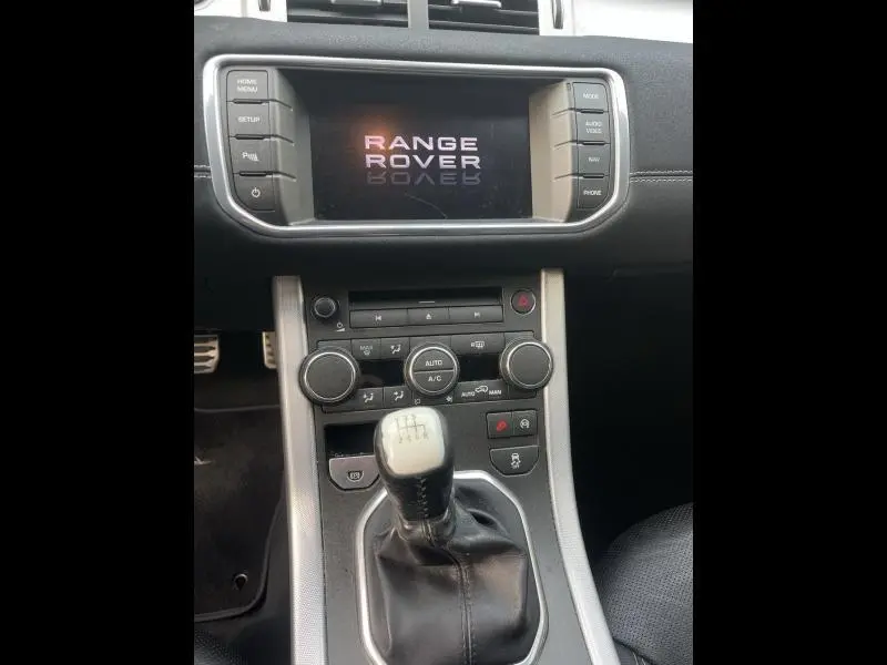 Gros plan intérieur sur la console centrale et levier de vitesse manuel du Range Rover Evoque gris Orkney, écran tactile allumé.