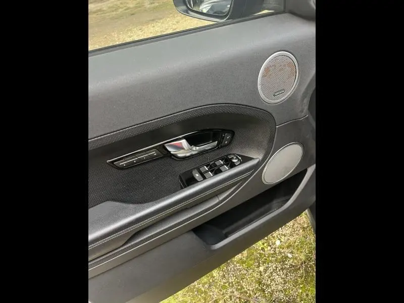 Intérieur côté gauche de la porte d’un Range Rover Evoque gris Orkney, avec commandes vitres et haut-parleurs ronds.