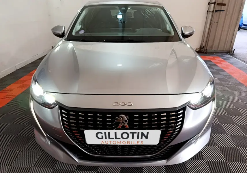 Vue frontale d'une Peugeot 208 gris clair avec phares LED allumés et calandre noire distinctive.