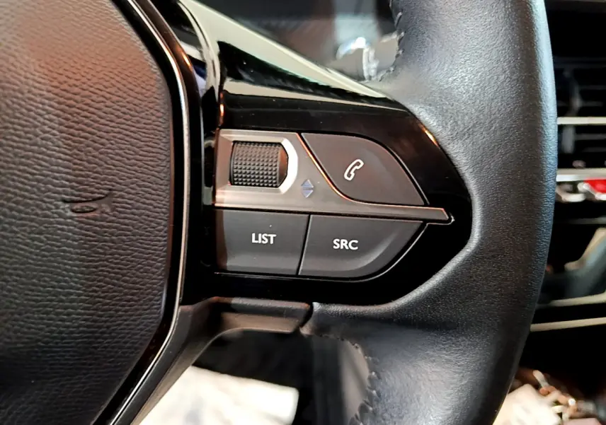 Gros plan sur les commandes gauche du volant cuir noir de la Peugeot 208 gris clair, avec boutons LIST et SRC visibles.