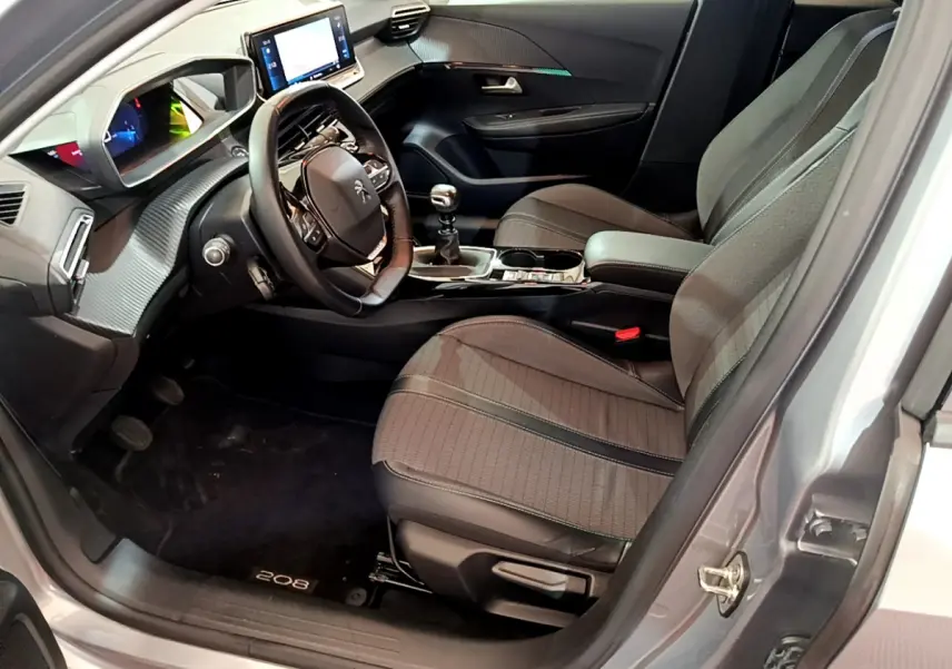 Intérieur de la Peugeot 208 gris clair vue côté conducteur, volant cuir et écran tactile central visible.