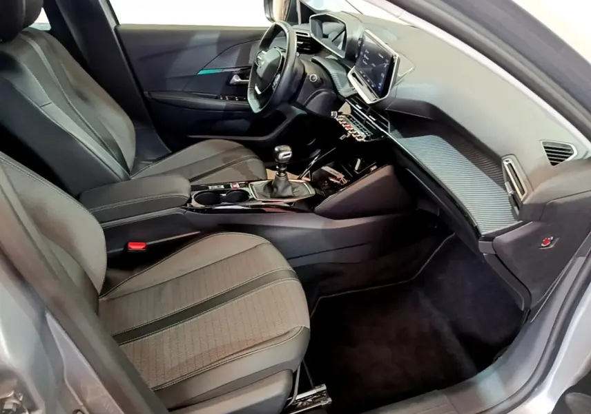 Intérieur avant droit de la Peugeot 208 gris clair 2020, avec tableau de bord moderne et boîte manuelle.