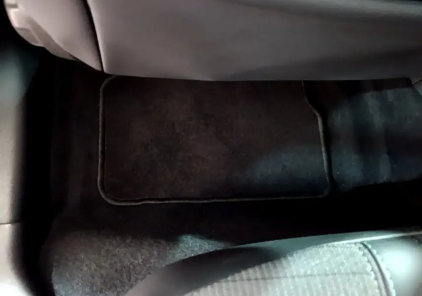 Gros plan sur le tapis de sol noir et le frein à main cuir dans l'habitacle d'une Peugeot 208 gris clair.