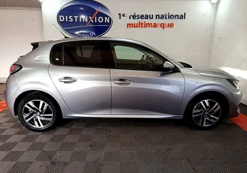 Profil côté gauche d'une Peugeot 208 gris clair 2020, avec jantes alliage et vitres teintées, en intérieur showroom.