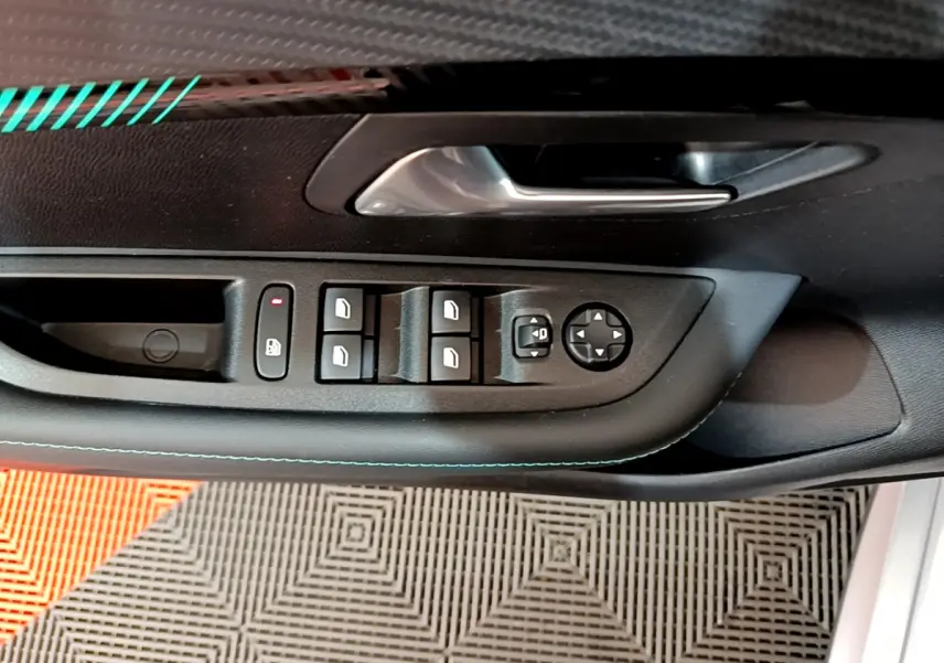 Vue rapprochée de la porte côté gauche d'une Peugeot 208 gris clair, montrant les commandes électriques des vitres et rétroviseurs.