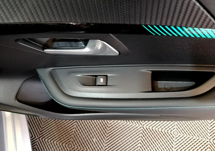 Gros plan sur la poignée intérieure côté conducteur de la Peugeot 208 gris clair avec surpiqûres bleues et bouton de vitre électrique.
