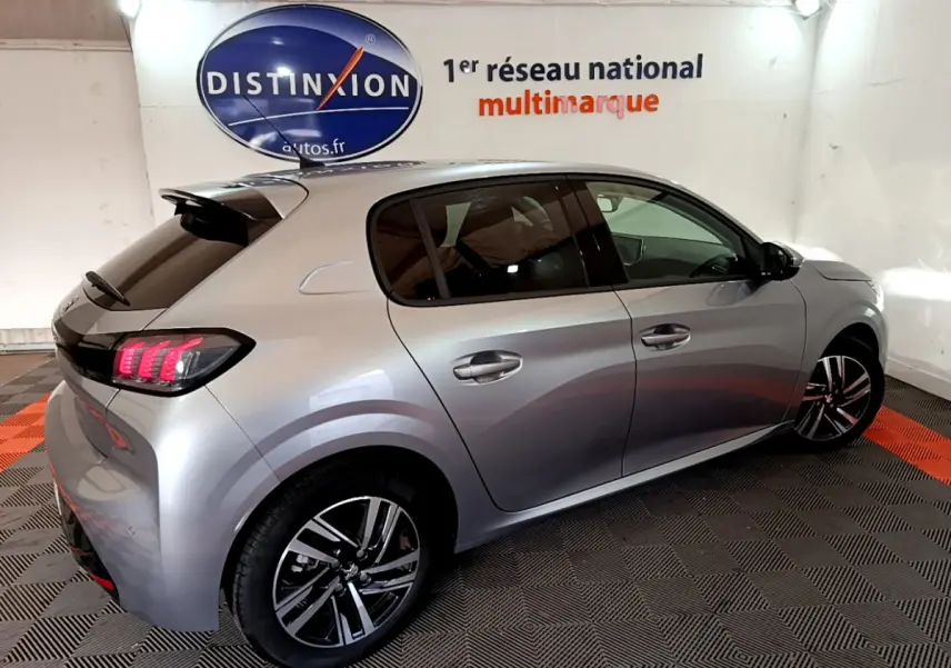Peugeot 208 gris clair vue de côté droit arrière, feux LED allumés et jantes alliage distinctives.