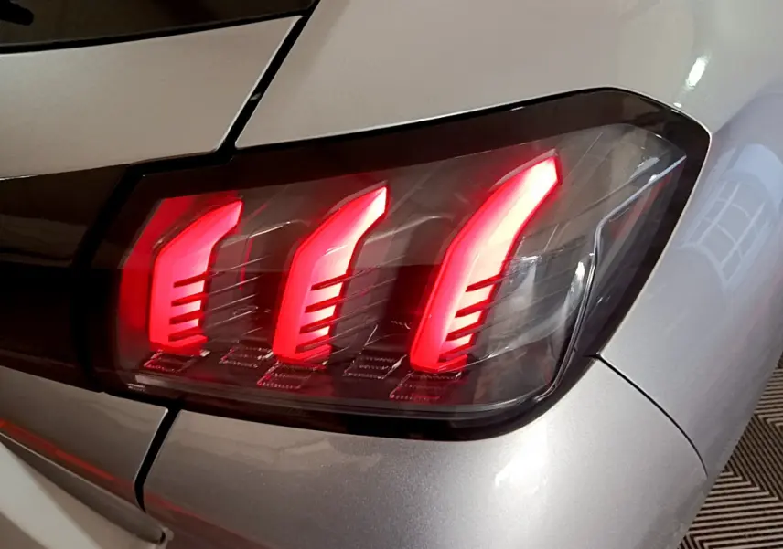 Gros plan sur le feu arrière droit rouge vif d'une Peugeot 208 gris clair, version PureTech 100 S&S Allure Business.