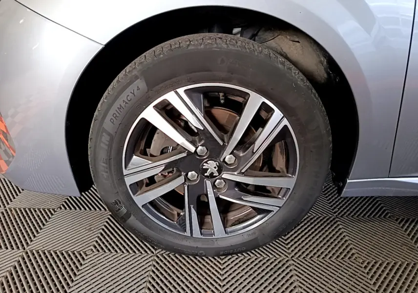 Gros plan sur la roue avant gauche gris clair de la Peugeot 208 avec jante alliage et logo lion au centre
