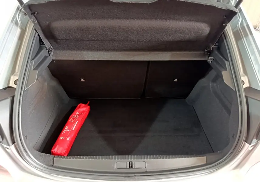 Coffre ouvert d'une Peugeot 208 gris clair, vue arrière montrant un espace de rangement propre avec une trousse de secours rouge.
