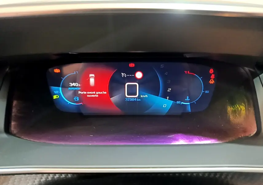 Affichage numérique du tableau de bord de la Peugeot 208 PureTech 100, indiquant porte avant gauche ouverte et vitesse à zéro.