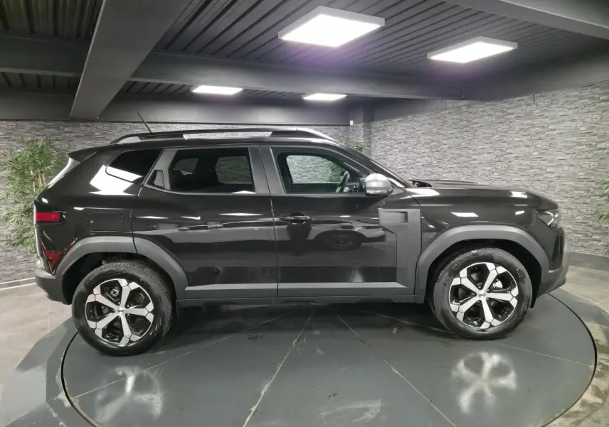 Profil droit du Dacia Duster 1.6 Hybrid 140 Journey noir nacré avec jantes alliage diamantées en intérieur showroom.