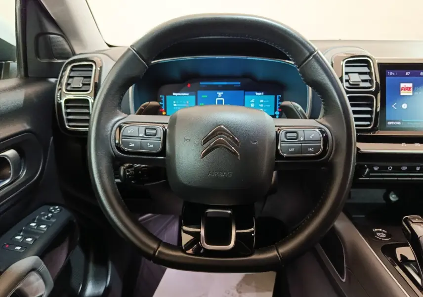 Vue intérieure centrée sur le volant noir du Citroën C5 Aircross Hybrid avec tableau de bord numérique et écran tactile.