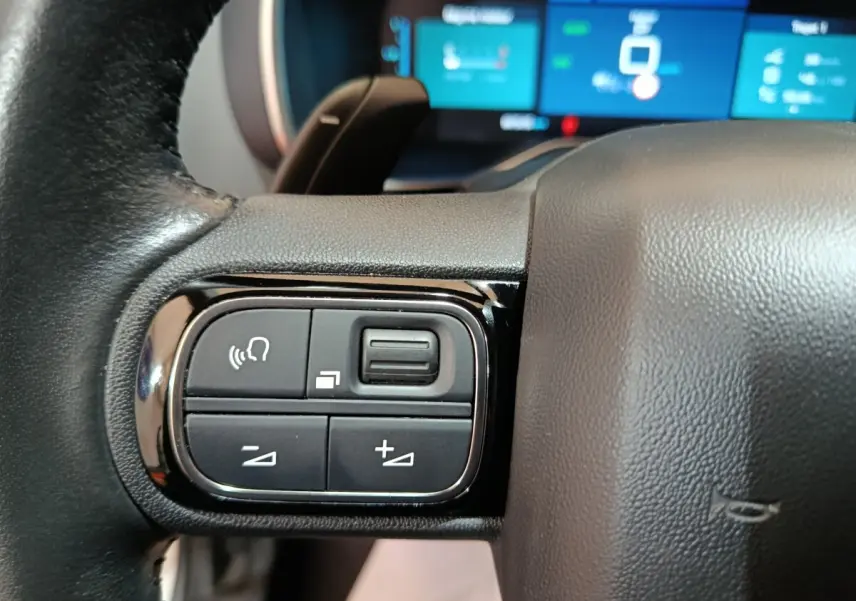 Gros plan sur les commandes multifonctions à gauche du volant du Citroën C5 Aircross Hybrid blanc, avec écran tactile en arrière-plan flou.