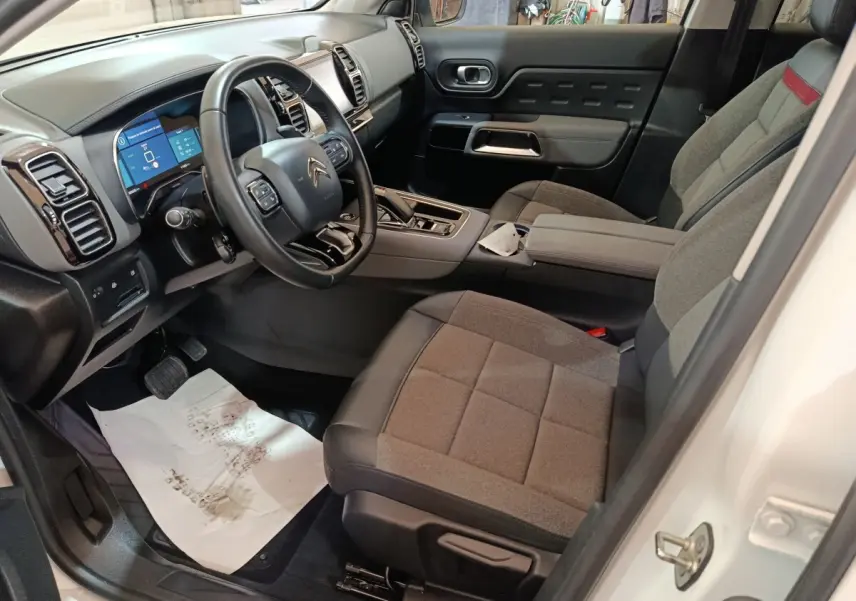 Intérieur côté conducteur du Citroën C5 Aircross Hybrid blanc, avec tableau de bord numérique et sièges gris tissu.