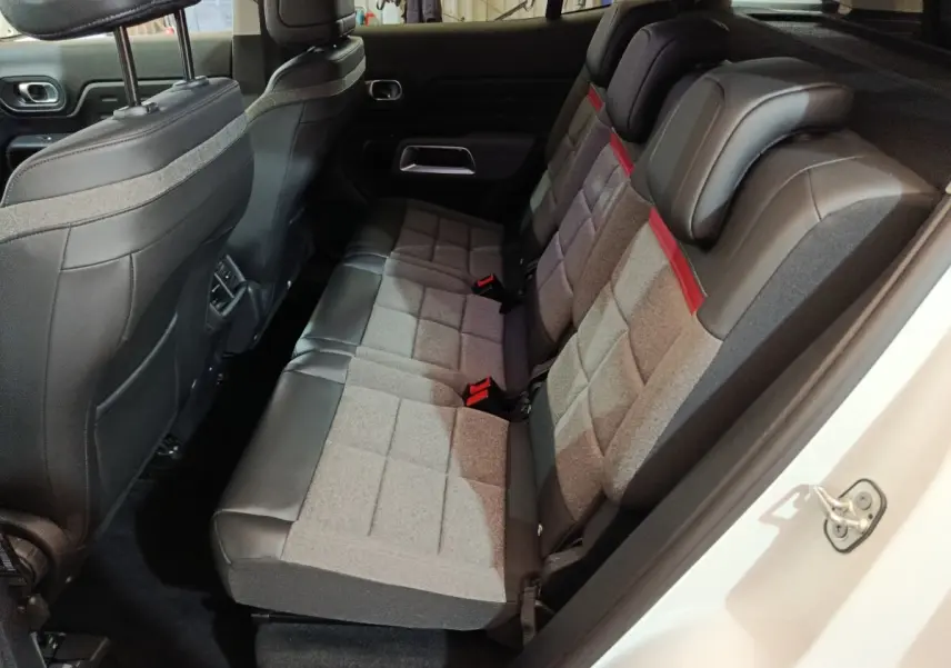 Vue intérieure côté droit sur les sièges arrière gris et noirs du Citroën C5 Aircross Hybrid blanc, avec appuie-têtes et ceinture rouge.