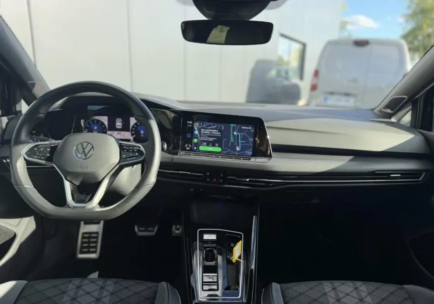 Vue intérieure avant de la Volkswagen Golf 8 noire, avec tableau de bord numérique et écran tactile central.