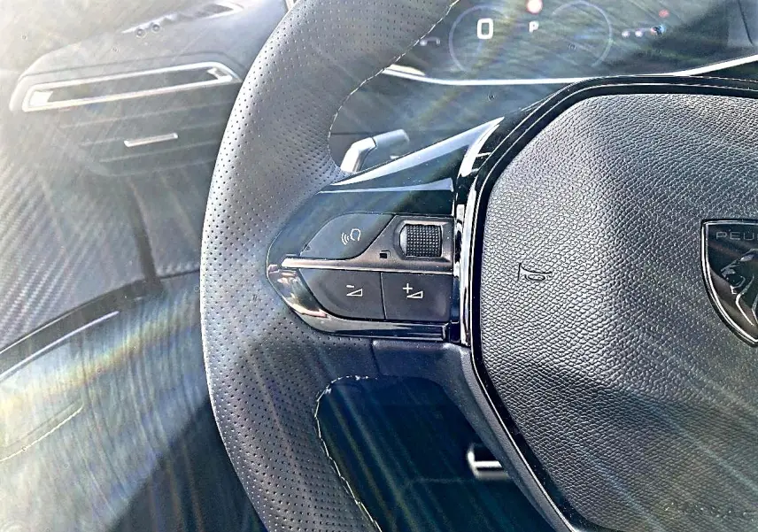 Gros plan sur le volant cuir perforé noir de la Peugeot 2008 1.2 hybrid 145 GT avec commandes intégrées.