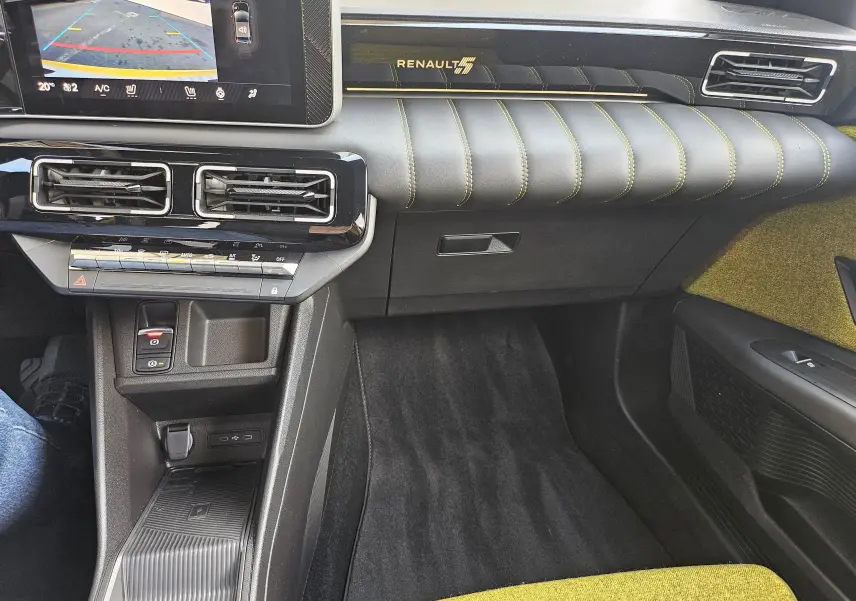 Vue intérieure côté passager de la Renault R5 Iconic 2025, tableau de bord noir avec surpiqûres jaunes et logo Renault éclairé.