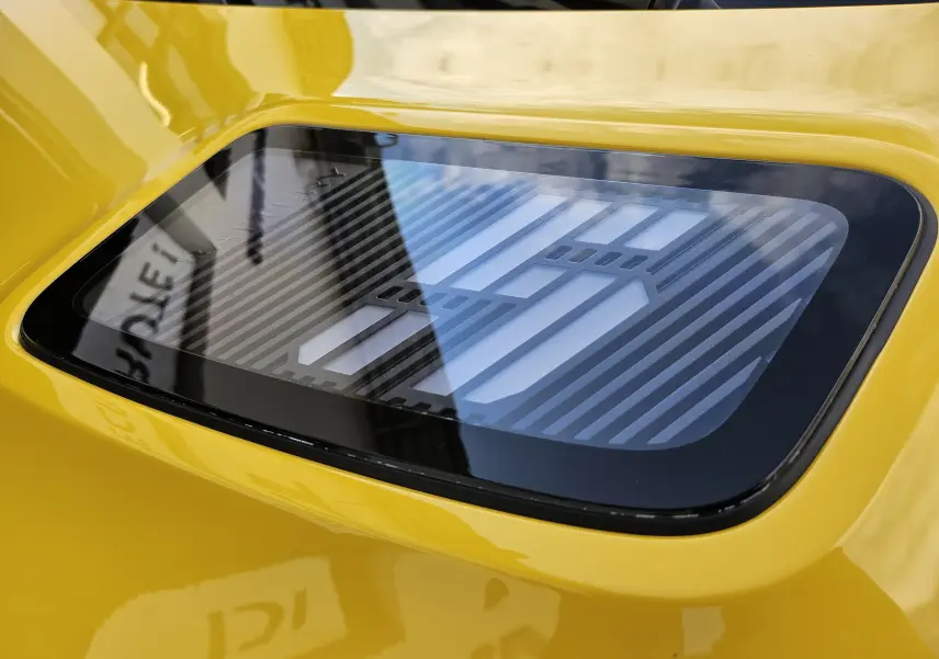 Gros plan sur le capot jaune pop de la Renault R5 électrique 2025 avec son logo stylisé sous vitre noire.