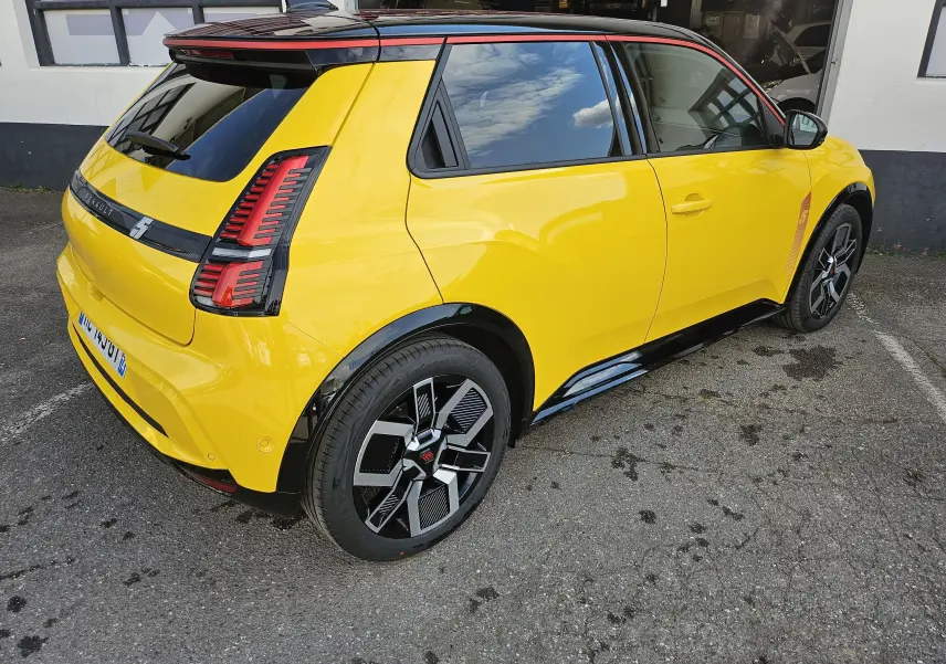 Vue 3/4 arrière droite d'une Renault R5 Iconic jaune pop avec toit noir et jantes noires distinctives.