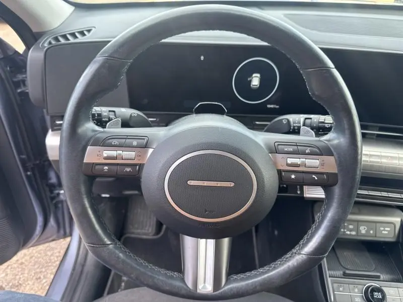Vue rapprochée du volant cuir multifonction noir du Hyundai KONA Electric 2023, avec tableau de bord numérique en arrière-plan.