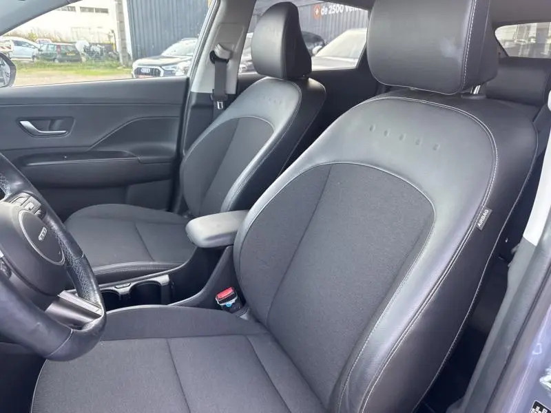 Vue intérieure côté conducteur du Hyundai Kona Electric 2023, sièges cuir-tissu noirs avec accoudoir central.