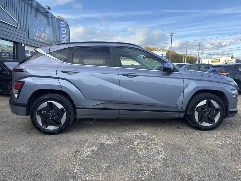 Vue de profil côté gauche d'un Hyundai Kona Electric 2023 Metal Blue métallisé avec jantes alu distinctives et vitres surteintées.
