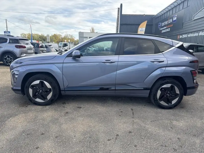 Profil côté gauche d'un Hyundai Kona Electric 2023 métallisé Metal Blue avec jantes alu et vitres surteintées.