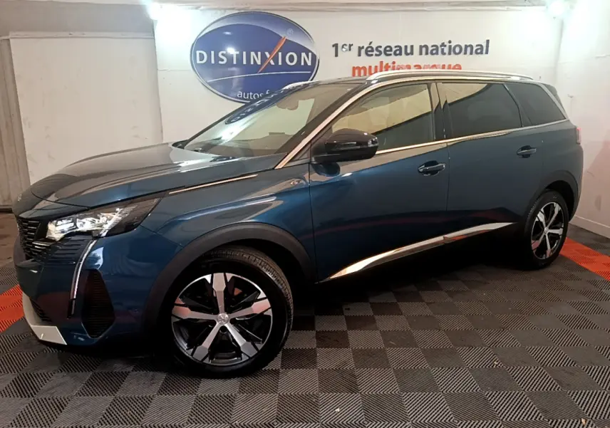 Vue de profil côté gauche d'un Peugeot 5008 bleu avec jantes alliage et vitres teintées dans un showroom intérieur.