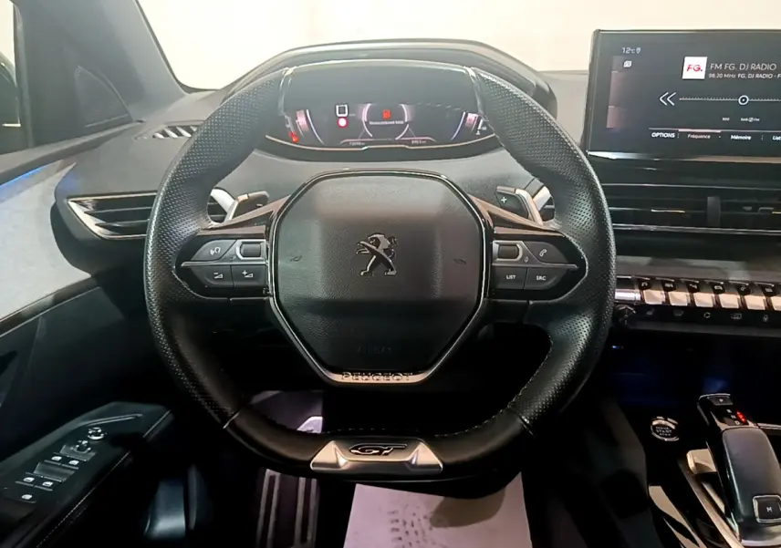 Vue rapprochée du volant cuir noir GT et tableau de bord numérique du Peugeot 5008 bleu 2021.