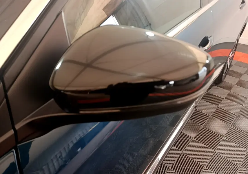 Rétroviseur droit noir brillant du Peugeot 5008 bleu, vue rapprochée côté passager sur sol à motifs.