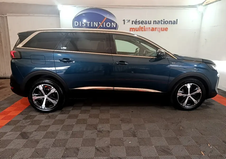 Profil côté droit d'un Peugeot 5008 GT bleu 2021 avec jantes alliage et toit noir en intérieur showroom
