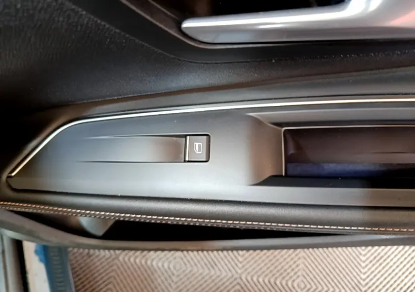 Gros plan sur la commande de lève-vitre côté conducteur, garniture noire avec surpiqûres blanches du Peugeot 5008 bleu.
