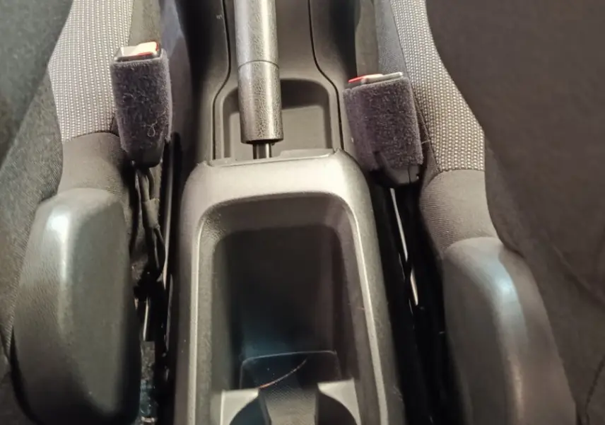 Vue rapprochée de la console centrale noire entre les sièges avant gris d'une Citroën C3 blanche, avec frein à main et porte-gobelet.