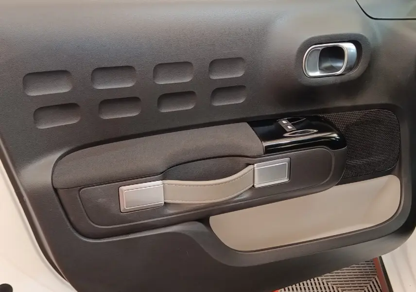 Gros plan sur la porte intérieure côté conducteur de la Citroën C3 blanche, avec poignée beige et commandes vitres noires.