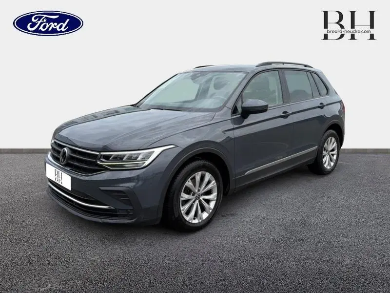 Volkswagen Tiguan 1.5 TSI gris dauphin métallisé vu en 3/4 avant droit avec jantes alu et barres de toit.