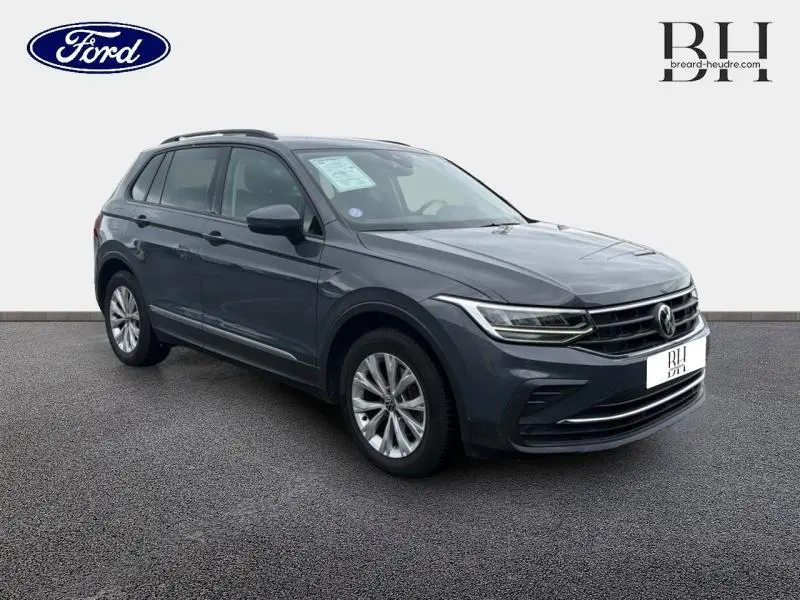 Vue 3/4 avant droite d’un Volkswagen Tiguan 1.5 TSI 150ch Life Business gris dauphin métallisé avec jantes alu et barres de toit.
