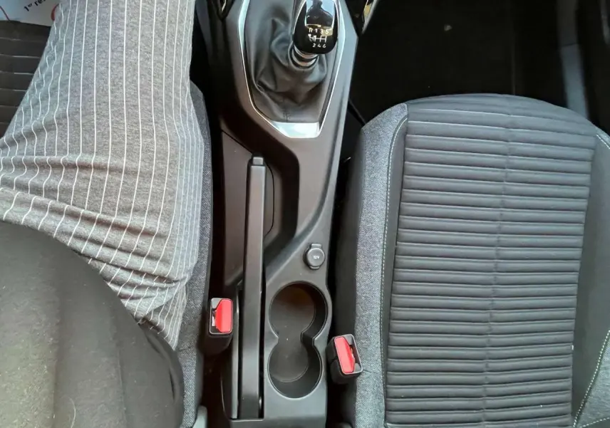 Vue plongeante sur la console centrale d'une Peugeot 2008 2024, boîte manuelle, sièges gris et boutons rouges des ceintures.