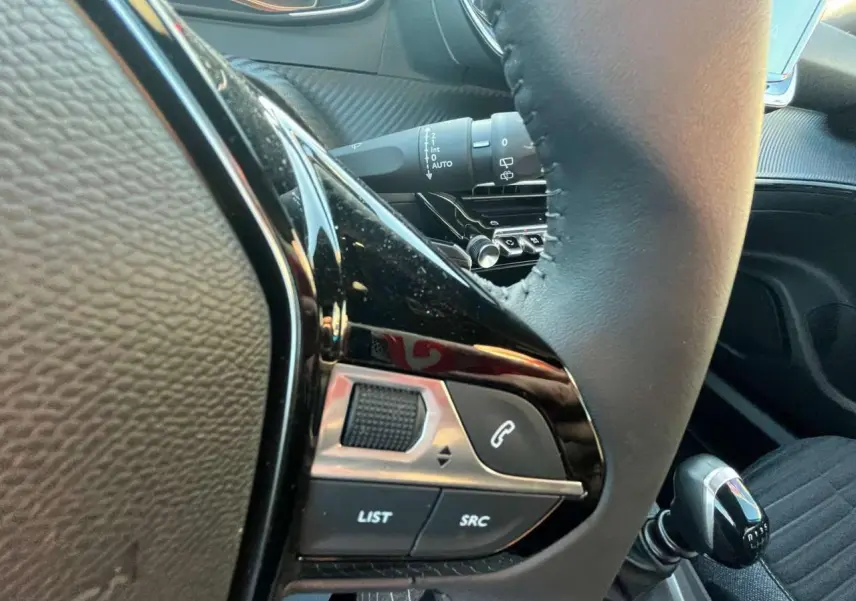 Gros plan sur les commandes au volant côté gauche du Peugeot 2008 2024, avec levier de vitesses manuel visible.