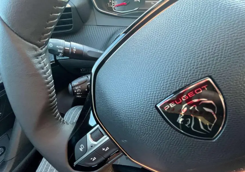 Gros plan sur le volant noir du Peugeot 2008 2024 avec logo lion et commandes intégrées, tableau de bord en arrière-plan.