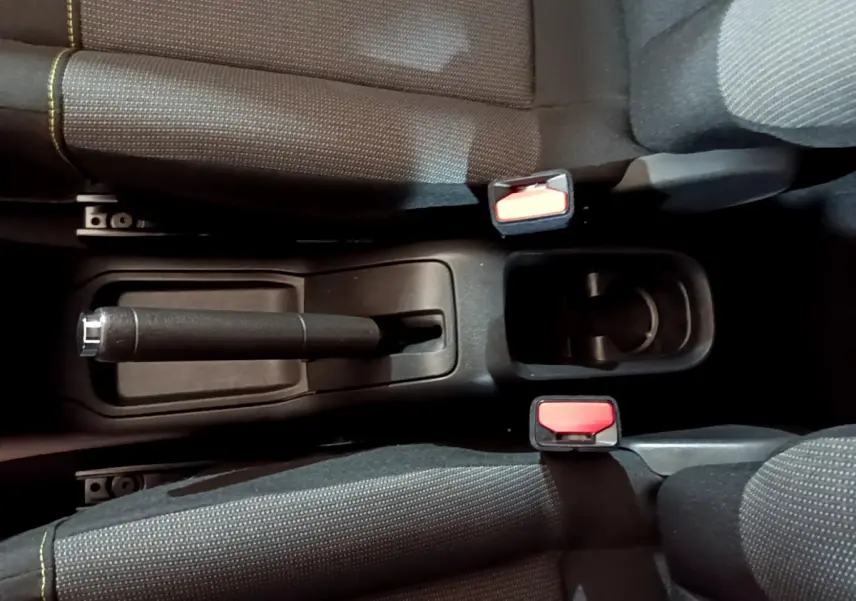 Vue plongeante sur la console centrale noire de la Citroën C3 avec frein à main manuel et deux ceintures rouges.