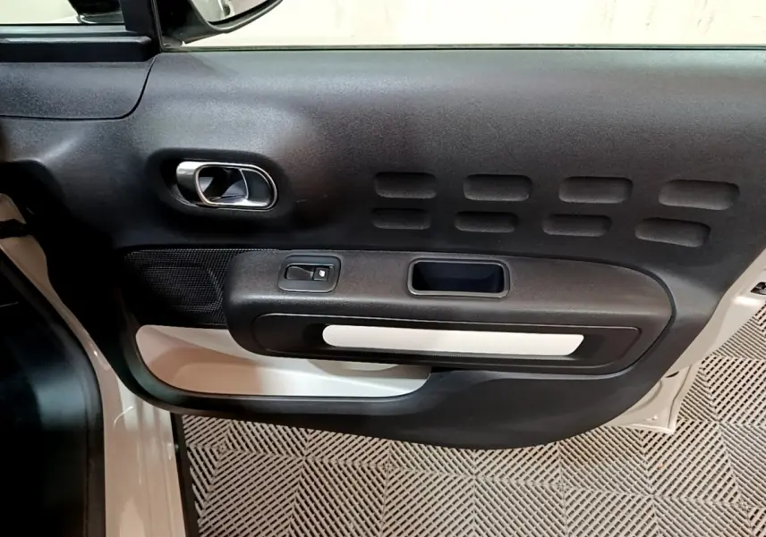 Vue rapprochée de la porte avant gauche beige de la Citroën C3 2022 avec poignée intérieure chromée et commande de vitre.