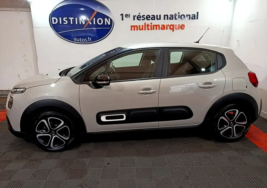 Profil côté gauche d'une Citroën C3 beige 2022 avec protections noires et jantes distinctives en intérieur showroom.