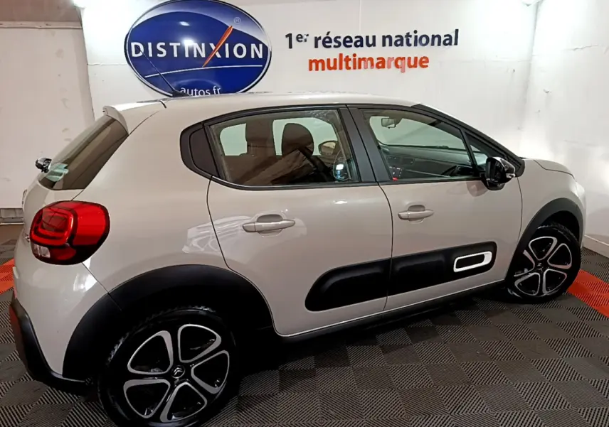 Profil côté gauche d'une Citroën C3 beige 2022 avec protections noires et jantes alliage stylisées en intérieur showroom.