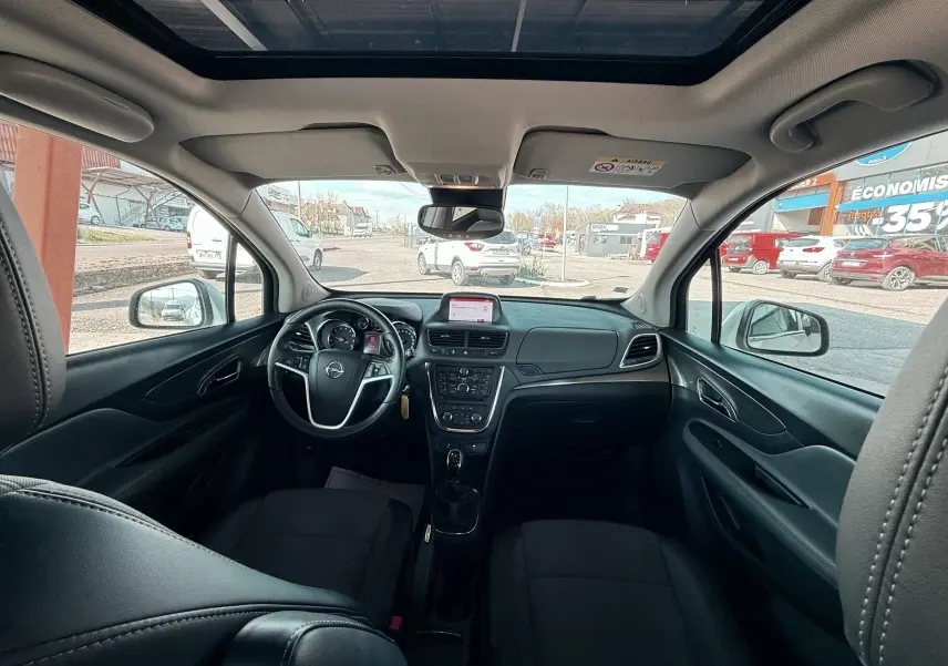 Vue intérieure avant de l’Opel Mokka X blanc, montrant le tableau de bord, le volant et le toit ouvrant panoramique.