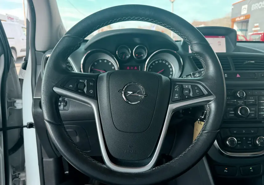 Vue centrée sur le volant en cuir noir de l’Opel Mokka X blanc, avec tableau de bord et commandes visibles.