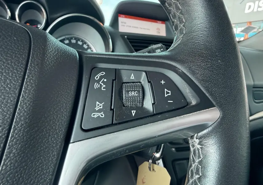 Gros plan sur les commandes audio au volant noir de l'Opel Mokka X blanc, avec tableau de bord en arrière-plan.