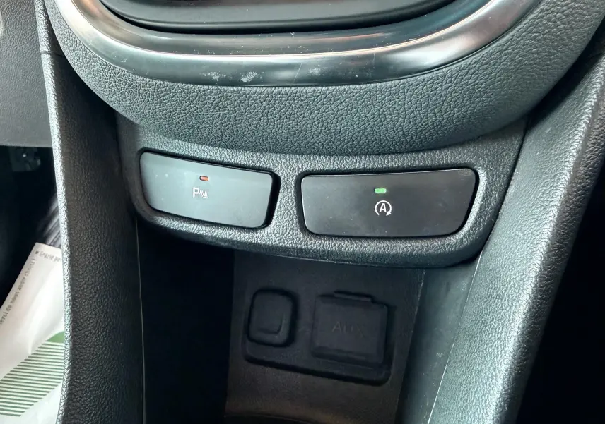 Gros plan sur les commandes de la console centrale noire de l’Opel Mokka X, avec boutons de stationnement et arrêt auto.