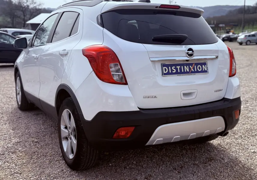 Vue 3/4 arrière gauche d’un Opel Mokka X blanc avec feux arrière rouges et plaque d’immatriculation Distinxion.